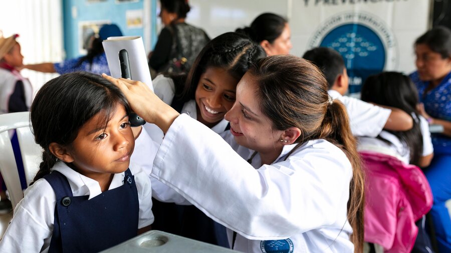 Voluntaria de la Fundación realizando una valoración médica a una niña en una brigada de salud escolar.