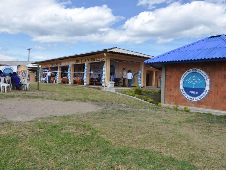 La sede de la Institución Educativa Departamental Indígena Misak después de la adecuación: un salón de ladrillo con techo azul y el escudo de la Fundación, junto a los demás bloques, el día de la entrega.