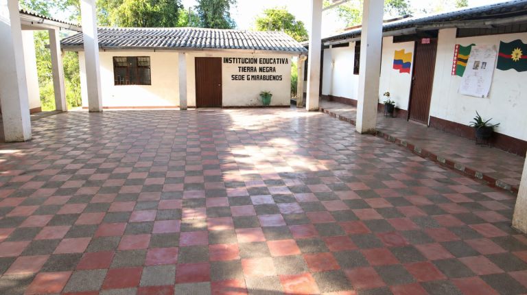 La sede antigua: un patio de baldosas rojas y grises rodeado de corredores con columnas, y en la pared el letrero «Institución Educativa Tierra Negra, Sede G Mirabuenos».