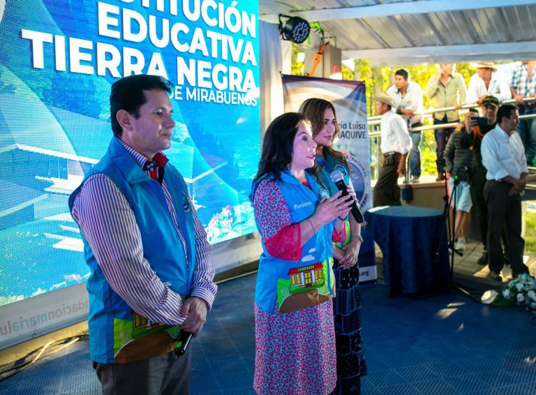 La Dra. María Luisa de Moreno habla con un micrófono frente a la pantalla que anuncia la inauguración de la sede Mirabuenos.