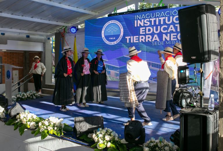 Estudiantes con trajes típicos santandereanos, sombreros y pañoletas rojas bailan en la tarima frente a la pantalla de la inauguración.