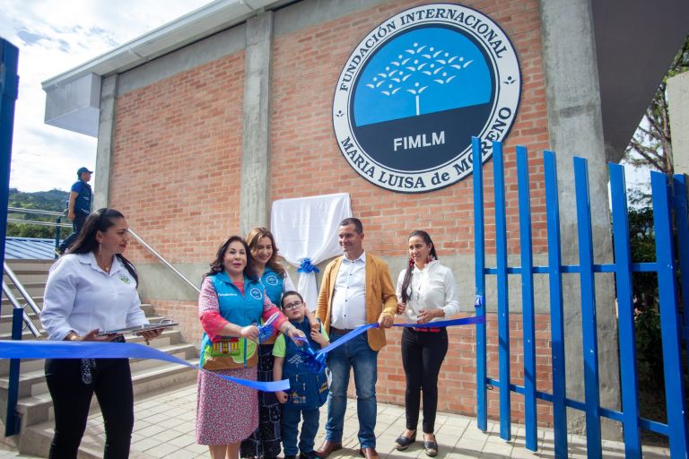 La Dra. María Luisa de Moreno corta la cinta azul en la entrada de la nueva sede, bajo el gran escudo de la Fundación pintado sobre el muro de ladrillo.