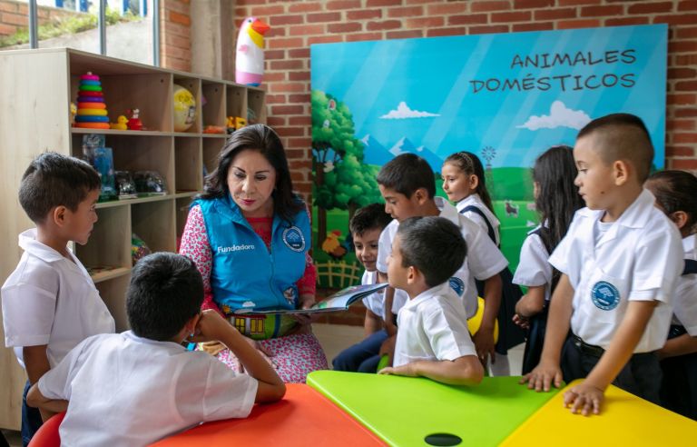 La Dra. María Luisa de Moreno lee un cuento a un grupo de niños junto al mural de animales domésticos del aula de preescolar.