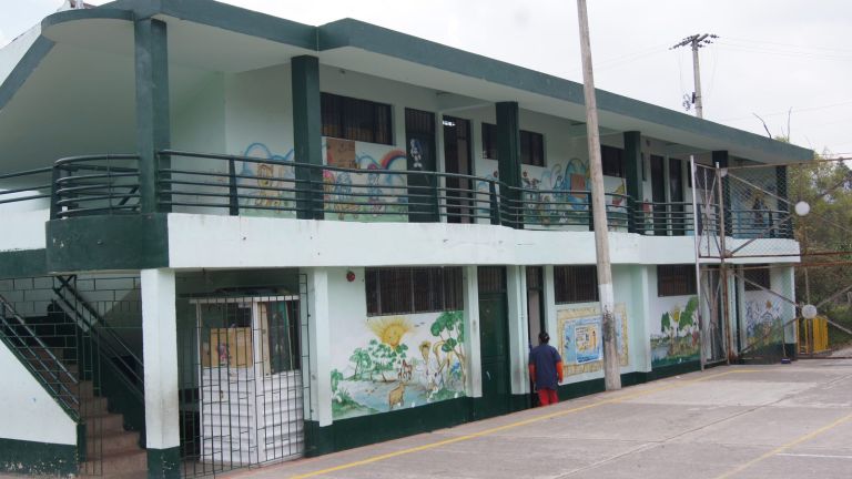 La sede antigua: un bloque de dos plantas pintado de verde y blanco, con murales infantiles en las paredes y rejas en las ventanas, frente a la cancha de cemento.