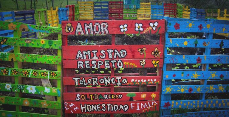 La huerta escolar hecha con estibas pintadas por los niños, con los valores escritos a mano: amor, amistad, respeto, tolerancia, solidaridad y honestidad.