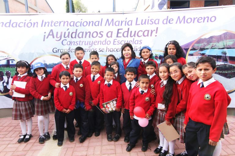 Un grupo grande de estudiantes con el uniforme rojo del colegio, posando frente al pendón de la campaña Ayúdanos a Educar.