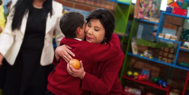 La Dra. María Luisa de Moreno abrazando a un estudiante que le entrega una manzana, en la ludoteca de la nueva sede.