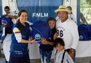 Una voluntaria de la Fundación entrega maletas escolares a una estudiante y su familia, bajo el pendón de la Fundación.