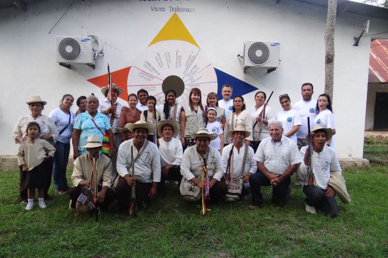 La comunidad y el equipo de voluntarios posan frente al mural de valores tradicionales de la escuela, con los mayores del cabildo al frente.