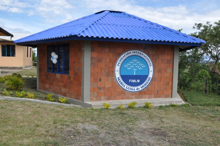 El nuevo salón de la escuela: muros de ladrillo a la vista, techo azul de cuatro aguas, ventana con reja azul y el sello de la Fundación en la fachada, rodeado de jardineras recién sembradas.