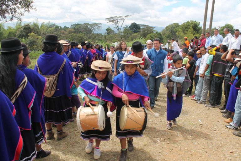 Niñas misak con tambores, un músico y un niño con flautas encabezan el recorrido por el camino de la escuela, con las montañas del Cauca al fondo.
