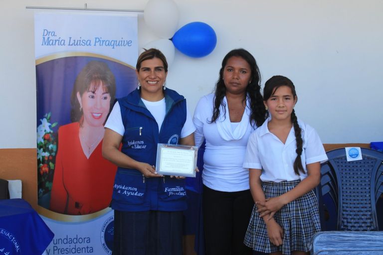 Una representante de la Fundación sostiene la placa de agradecimiento de la Escuela Suer de Navas, de la vereda Palo Blanco, por la adecuación de la escuela, junto a una docente y una estudiante.