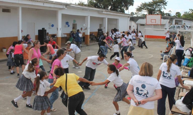 Estudiantes, madres y voluntarios de la Fundación juegan tomados de las manos en la cancha, frente a las aulas recién pintadas de blanco y naranja.
