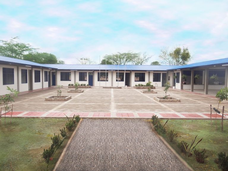 La sede terminada: aulas de muros blancos y techos azules alrededor de una plazoleta adoquinada con jardineras y astas para las banderas.