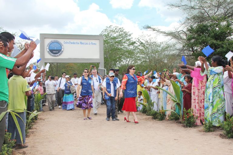 La Dra. María Luisa de Moreno y el equipo de la Fundación llegan a la escuela por un camino flanqueado por la comunidad wayuu, que los recibe agitando banderas azules y blancas.