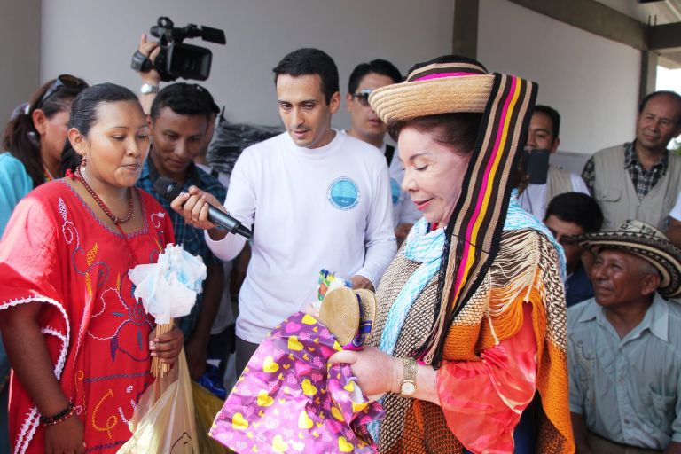 Una mujer wayuu entrega regalos tejidos por la comunidad, entre ellos un sombrero y una mochila, a una representante de la Fundación.