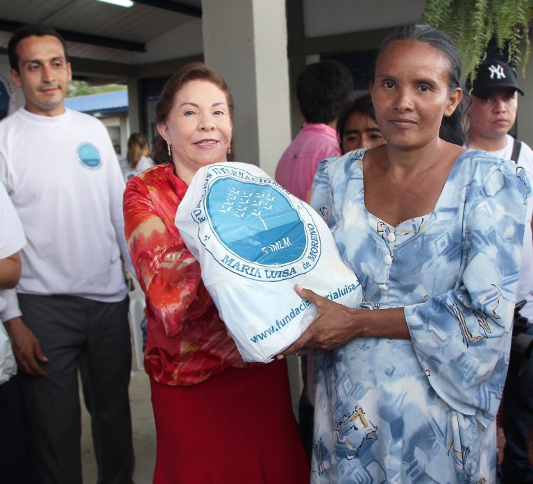 Una representante de la Fundación entrega un paquete a una madre de la comunidad en el corredor de la nueva escuela.