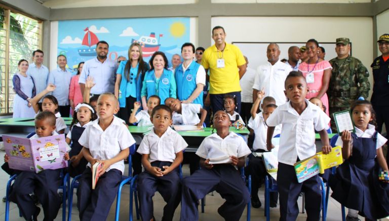 Los estudiantes, con uniforme blanco y azul, estrenan su aula con libros en las manos, rodeados por el equipo de la Fundación y las autoridades el día de la entrega.