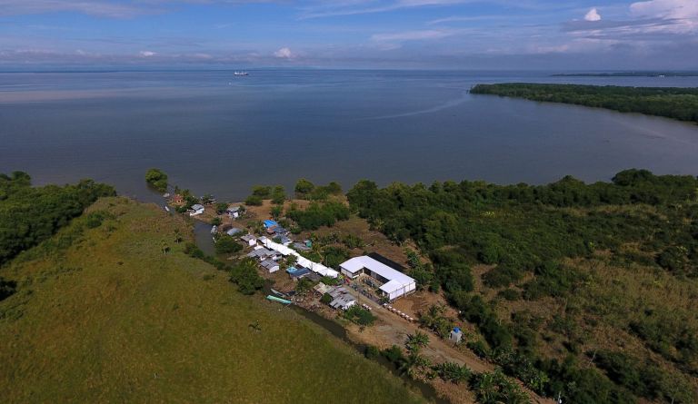 Vista aérea de la escuela junto al caserío de Puerto Bello, entre manglares y a orillas del golfo de Urabá, con un barco a lo lejos.