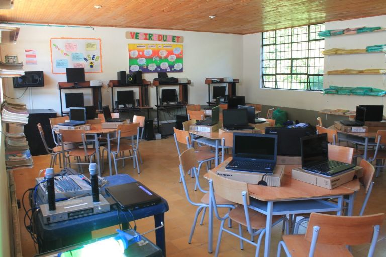 La sala de sistemas dotada: computadores portátiles nuevos sobre las mesas, junto a sus cajas, equipos de escritorio al fondo y un equipo de sonido con micrófonos.