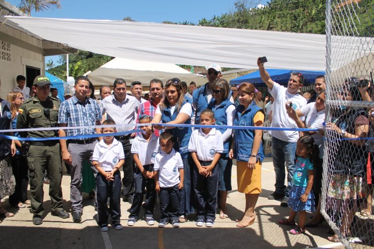 Corte de la cinta de inauguración en la cancha renovada, con cuatro niños de uniforme nuevo al frente, representantes de la Fundación, autoridades y la comunidad.