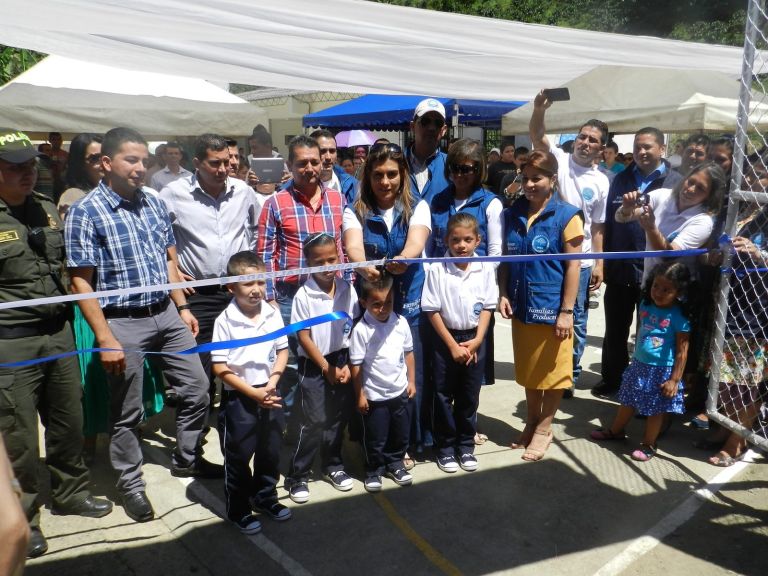 Otro momento del corte de cinta: una representante de la Fundación corta la cinta azul rodeada por los niños de uniforme, mientras los asistentes toman fotos.