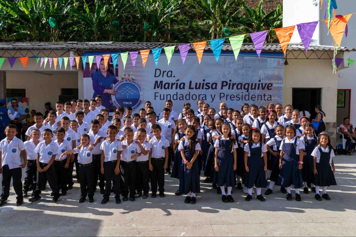 La escuela después: la fachada pintada de blanco y decorada con banderines de colores, con los estudiantes de uniforme posando frente a un pendón de la Fundación.