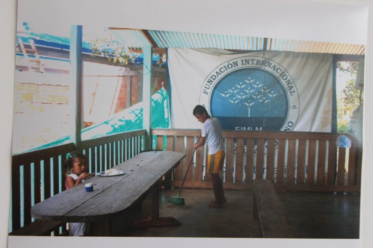 El comedor del antiguo albergue, con una mesa larga de tablas y una niña comiendo mientras un niño barre, bajo el pendón de la Fundación.