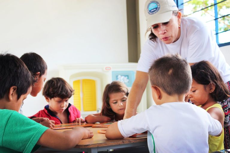 Una voluntaria de la Fundación acompaña a un grupo de niños que leen sus libros alrededor de una mesa en el aula nueva.