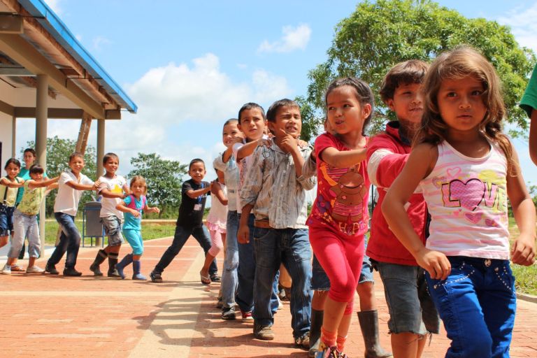 Los niños juegan al tren tomados de los hombros por la plazoleta de ladrillo, junto a las aulas nuevas.