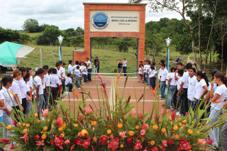 El portal de la nueva sede adornado con un gran arreglo de flores tropicales y frutas, entre dos filas de estudiantes con camisetas blancas, el día de la inauguración.