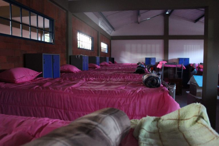 El nuevo dormitorio de las niñas, con camas de cobijas rosadas, casilleros azules y ventanas sobre muros de ladrillo.
