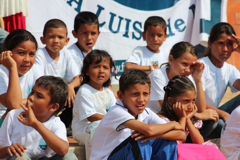 Niños con camisetas de la Fundación siguen atentos la ceremonia de inauguración, sentados en las gradas.
