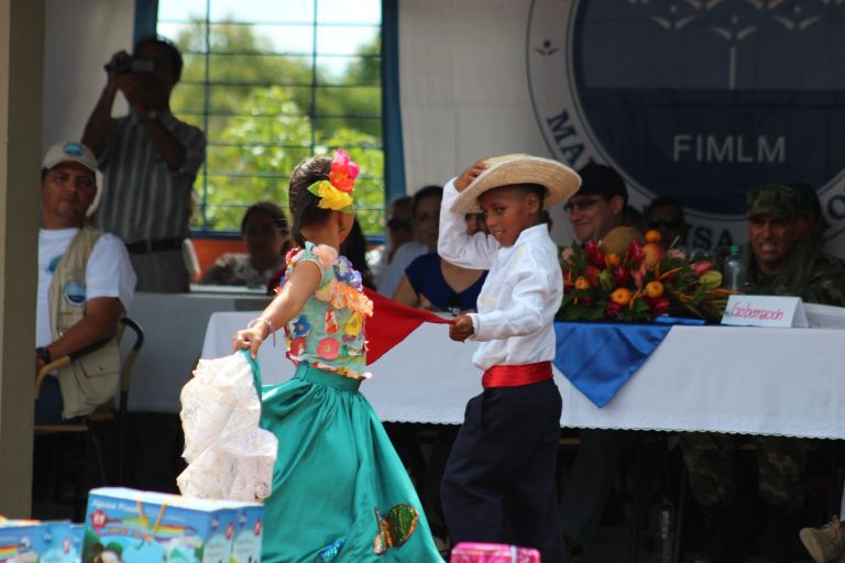 Dos niños con trajes típicos bailan frente a la mesa principal de la ceremonia, adornada con flores y frutas.