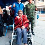 Una mujer en silla de ruedas junto a un militar y un voluntario de la Fundación sonriendo por haber recibido atención médica por personal militar.