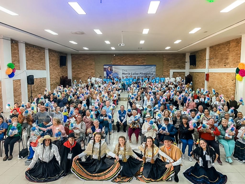 La fotografía captura un evento en el que personas se reúnen para celebrar la inclusión, los valores y la felicidad en Kennedy, Bogotá. En la imagen, se ven rostros sonrientes, gestos de camaradería y una atmósfera de alegría. Al fondo, se distinguen detalles como los voluntarios encargados del evento, pendón alusivo a la Dra. Maria Luisa y el logo de la FIMLM. La Fundación Internacional María Luisa de Moreno (FIMLM) está detrás de esta iniciativa, promoviendo un ambiente positivo y de apoyo mutuo.
