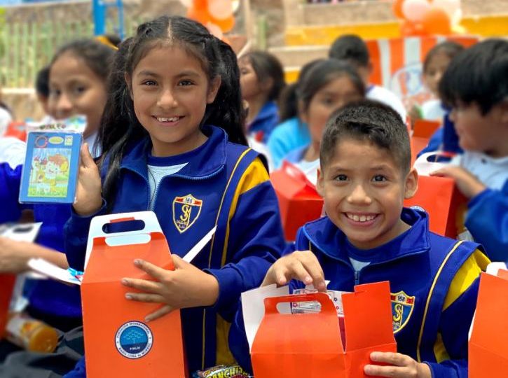 Una niña y un niño miran a la cámara sonríen mostrando sus regalos, una cajita con palomitas de maíz, un juego didáctico y el refresco para ver el Tele cine