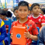 Un niño mira a la cámara sonríe mostrando su regalo, una cajita con palomitas de maíz, un juego didáctico y el refresco para ver el Tele cine