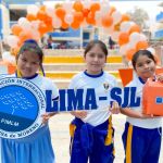 Tres niñas felices miran a la cámara sonriendo felices de recibir los regalos de la Fundación, una de ellas sostiene el logo de la Fundación, otra el nombre de Lima SJL y la ultima niña con el regalo.