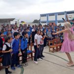 Todos los niños puestos de pie están participando a ritmo de la música en un juego lúdico propuesto por los animadores