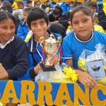 Dos niñas y un niño están posando con el marco decorativo de fundación que ellos mismos elaboraron, algunos muestran sus regalos