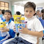 Un niños muy feliz muestra el regalo que le entrega la fundación, un juego didáctico, un refresco y palomitas de maíz