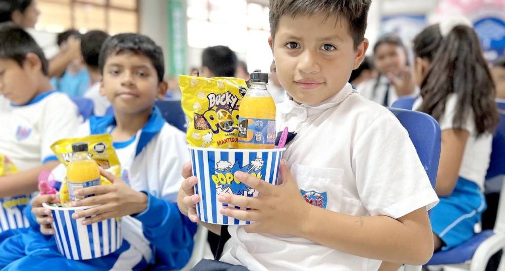 Un niños muy feliz muestra el regalo que le entrega la fundación, un juego didáctico, un refresco y palomitas de maíz