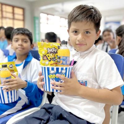 Un niños muy feliz muestra el regalo que le entrega la fundación, un juego didáctico, un refresco y palomitas de maíz