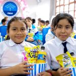 Dos niñas muy felices muestran el regalo que les entrega la fundación, un juego didáctico, un refresco y palomitas de maíz