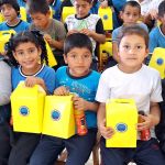 Dos niñas y un niño felices muestran su cajita sorpresas y sus refrigerios.