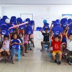 El grupo total de niños ponen en alto las mochilas que recibieron