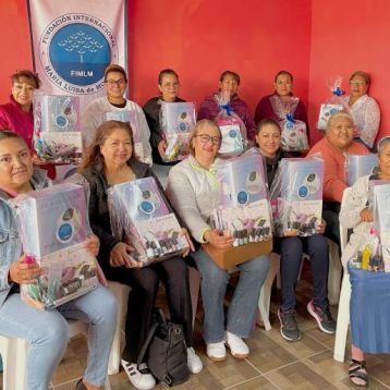 un grupo de mujeres beneficiarias sonrientes que sostienen orgullosamente kits de emprendimiento en belleza y cuidado personal, los cuales contienen productos como esmaltes, limas, lámparas UV y otros implementos.