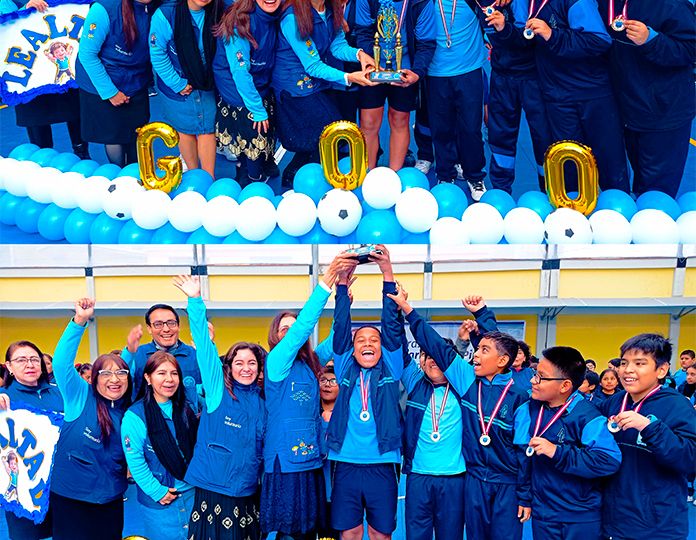El equipo de futbol en compañía de los voluntarios levantan el trofeo