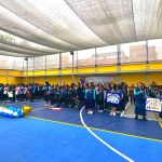 Niños y niñas están formados en el patio del colegio cantando el himno nacional
